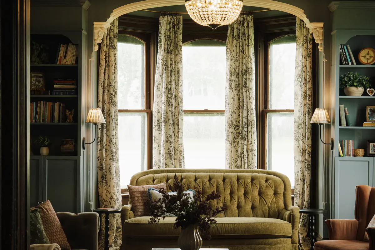 Sitting room with blue-green built-in bookshelves, toile curtains, and a tufted green velvet sofa