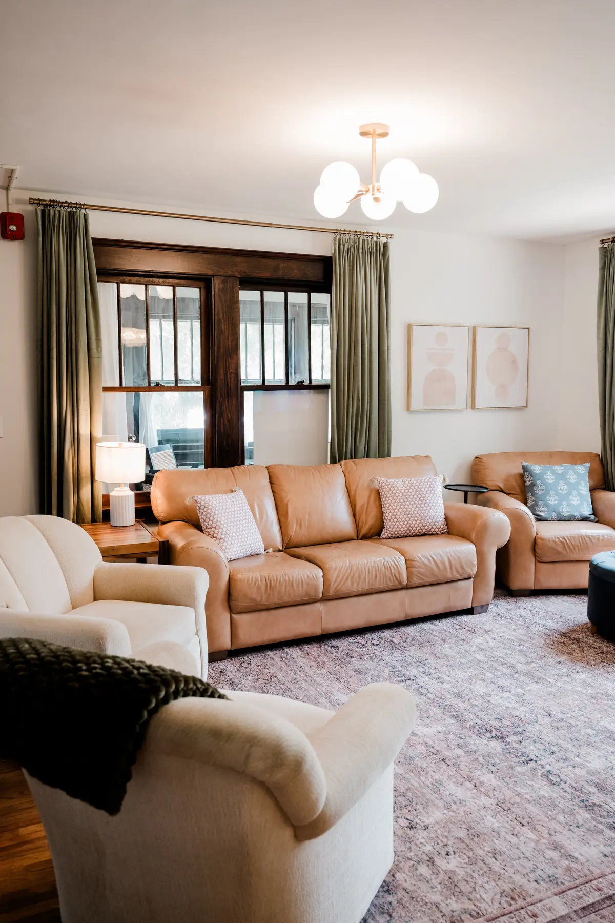 Living room with a cognac leather sofa, sage green walls, and dark-stained window trim