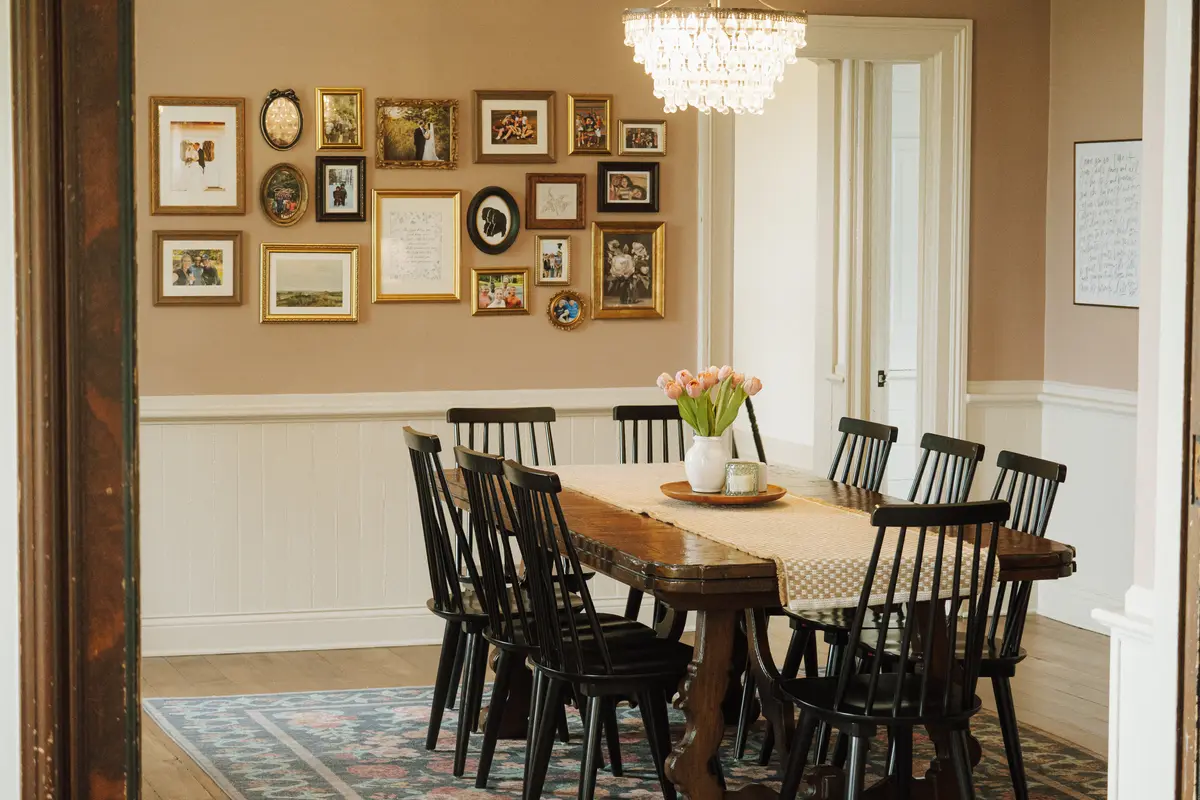 Dining room with a gallery wall of gold frames, a crystal chandelier, and black spindle chairs